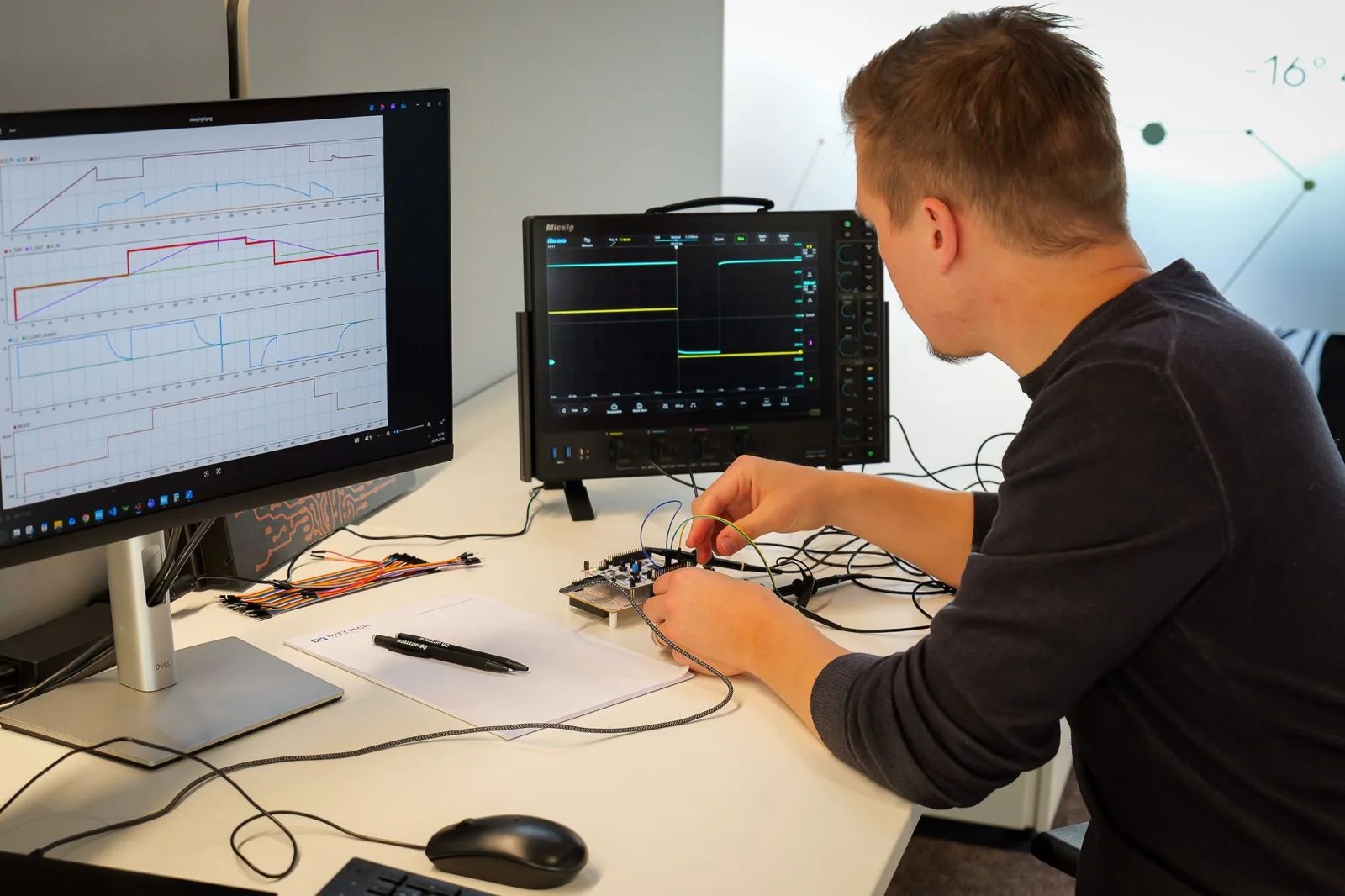 Embedded development at the bench: a controller board being wired up while an oscilloscope shows its signals